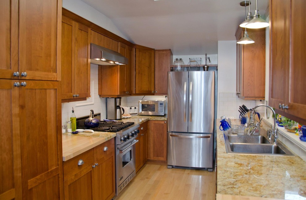 Amerikansk inredning av ett kök, med en undermonterad diskho, skåp i shakerstil, skåp i mellenmörkt trä, granitbänkskiva, vitt stänkskydd, stänkskydd i tunnelbanekakel och rostfria vitvaror