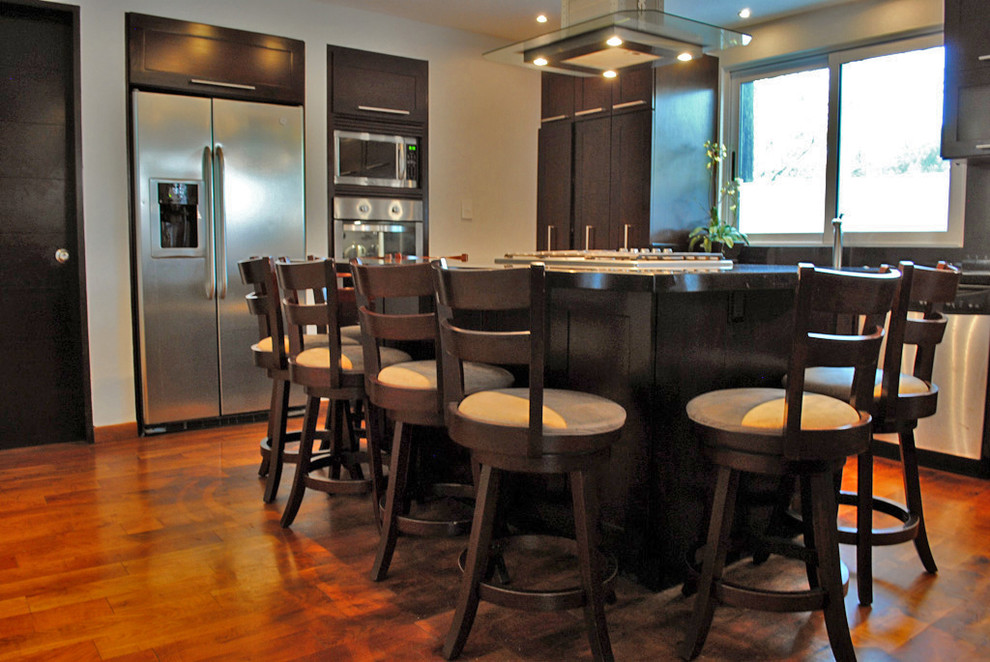 Photo of a contemporary u-shaped kitchen/diner in Mexico City with a submerged sink, recessed-panel cabinets, dark wood cabinets, granite worktops, black splashback and stainless steel appliances.