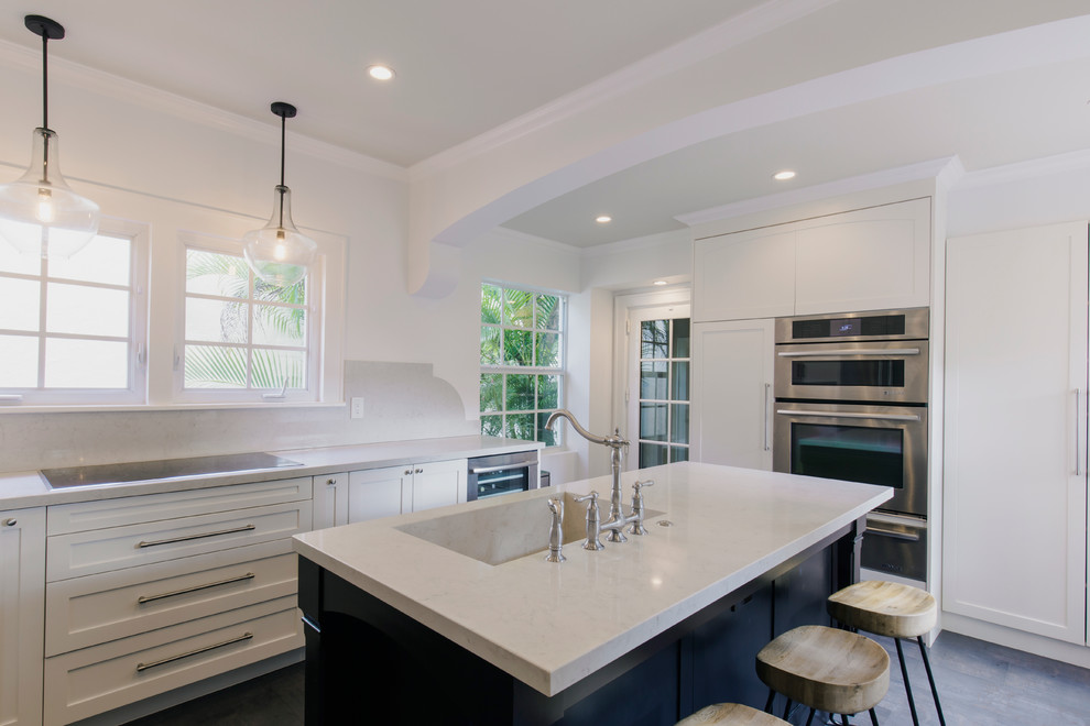 Inspiration for a mid-sized l-shaped dark wood floor enclosed kitchen remodel in Miami with an integrated sink, shaker cabinets, white cabinets, solid surface countertops, white backsplash, stone slab backsplash, stainless steel appliances and an island