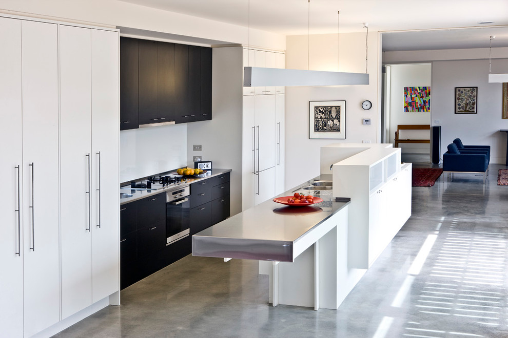 Example of a mid-sized minimalist galley concrete floor and gray floor open concept kitchen design in Canberra - Queanbeyan with a double-bowl sink, flat-panel cabinets, white cabinets, stainless steel countertops, white backsplash, an island and white countertops