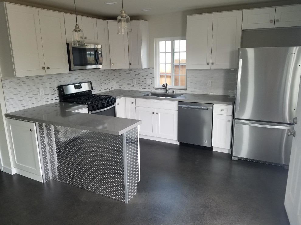 Foto på ett litet industriellt grå kök, med en undermonterad diskho, skåp i shakerstil, vita skåp, bänkskiva i kvarts, vitt stänkskydd, stänkskydd i porslinskakel, rostfria vitvaror, betonggolv, en halv köksö och grått golv