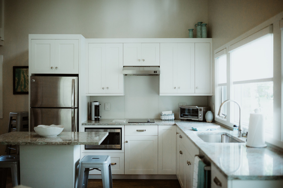 Aménagement d'une cuisine américaine moderne de taille moyenne avec des portes de placard blanches, un électroménager en acier inoxydable, parquet foncé, îlot, un sol marron et un plan de travail gris.