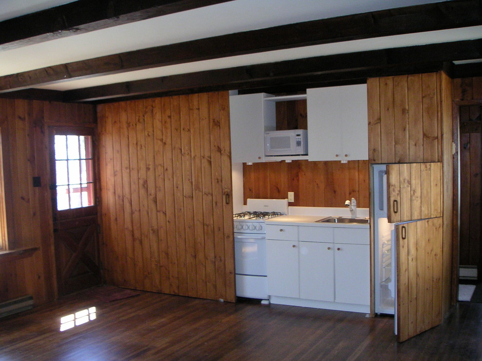 Diseño de cocina lineal rural pequeña abierta sin isla con armarios con paneles lisos, puertas de armario blancas, electrodomésticos blancos y suelo de madera oscura