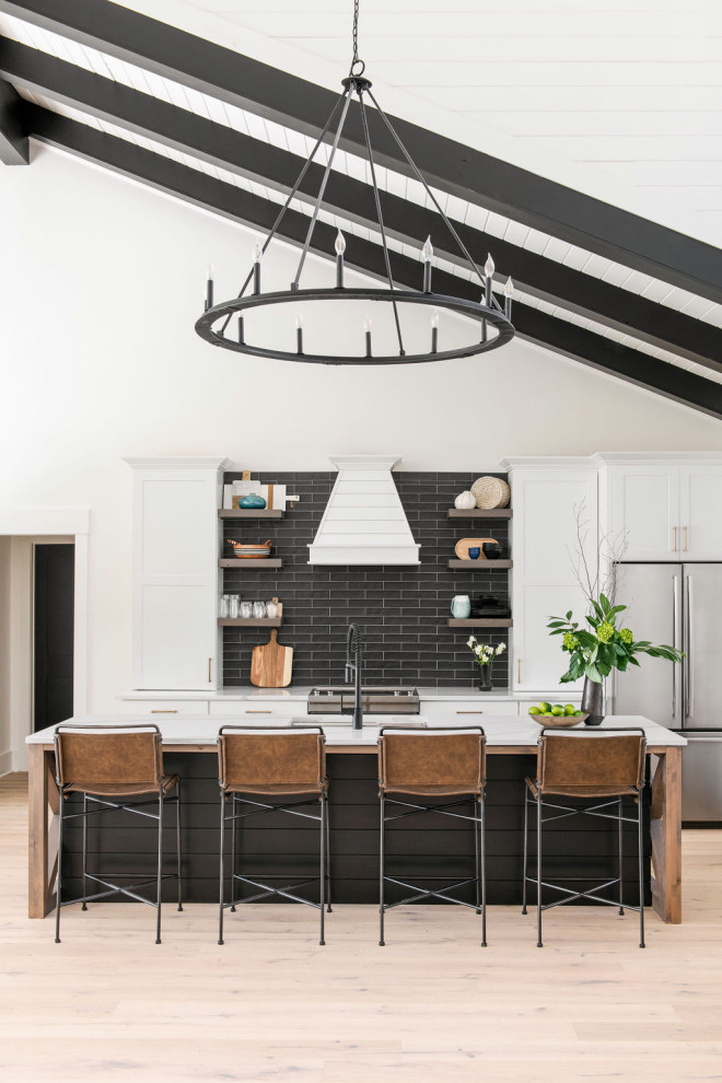 Inspiration for a large country single-wall light wood floor, brown floor and vaulted ceiling kitchen remodel in Charleston with an undermount sink, white cabinets, black backsplash, stainless steel appliances, an island and white countertops