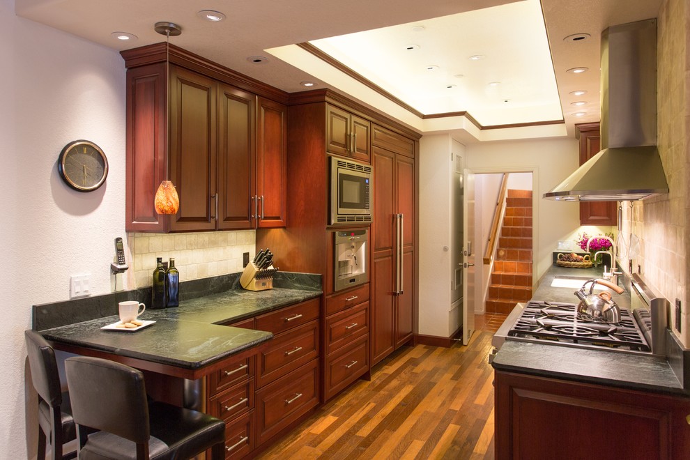 Example of a mid-sized tuscan galley laminate floor eat-in kitchen design in San Luis Obispo with an undermount sink, raised-panel cabinets, medium tone wood cabinets, soapstone countertops, beige backsplash, subway tile backsplash and paneled appliances