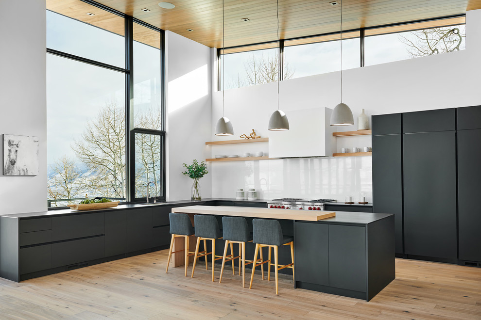 Large trendy u-shaped light wood floor and beige floor eat-in kitchen photo in Denver with a double-bowl sink, flat-panel cabinets, black cabinets, soapstone countertops, white backsplash, stone slab backsplash, paneled appliances, an island and black countertops