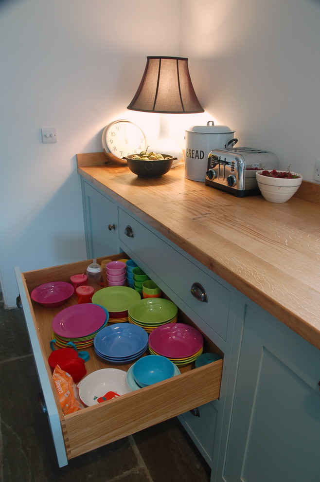 Foto på ett mellanstort kök, med en dubbel diskho, släta luckor, blå skåp, träbänkskiva, vitt stänkskydd och skiffergolv