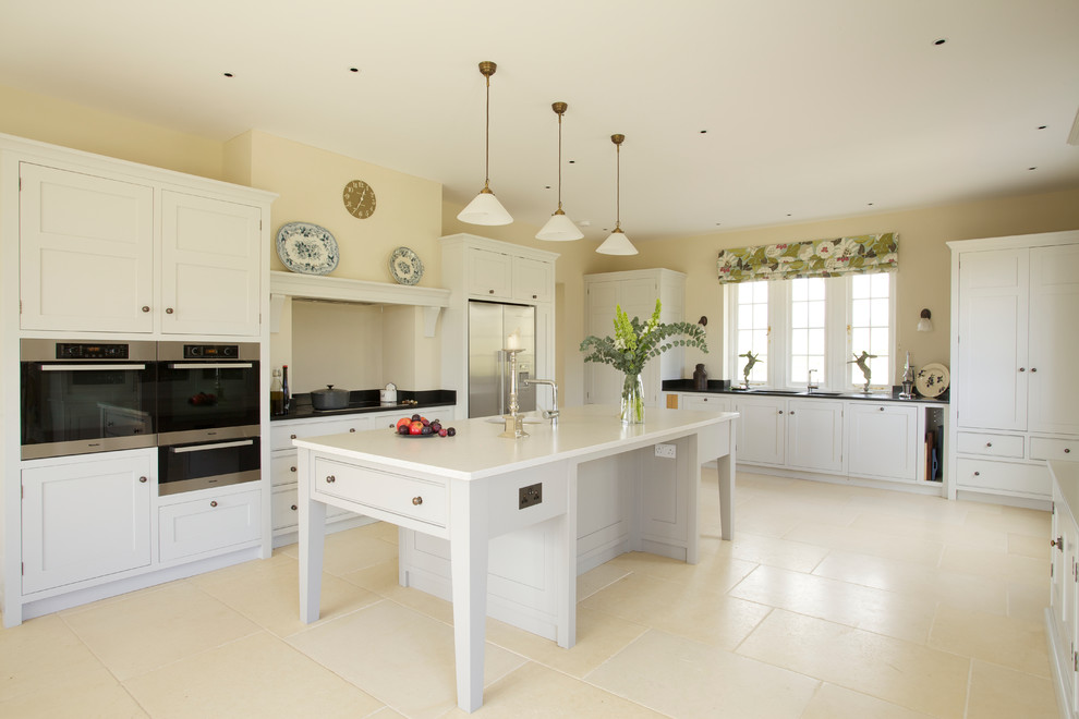 Photo of a large rural u-shaped kitchen in Wiltshire with a submerged sink, shaker cabinets, white cabinets, stainless steel appliances, an island and beige floors.