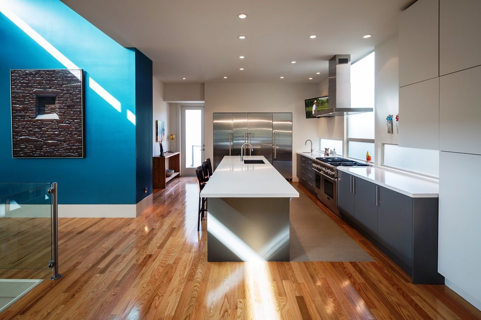 Foto på ett stort funkis kök, med en undermonterad diskho, släta luckor, grå skåp, rostfria vitvaror, mellanmörkt trägolv, en köksö, bänkskiva i koppar, vitt stänkskydd och brunt golv