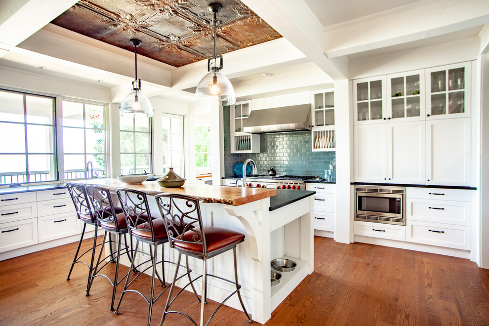 Eat-in kitchen - mid-sized coastal u-shaped medium tone wood floor and brown floor eat-in kitchen idea in Vancouver with an undermount sink, shaker cabinets, white cabinets, wood countertops, blue backsplash, ceramic backsplash, stainless steel appliances, an island and brown countertops