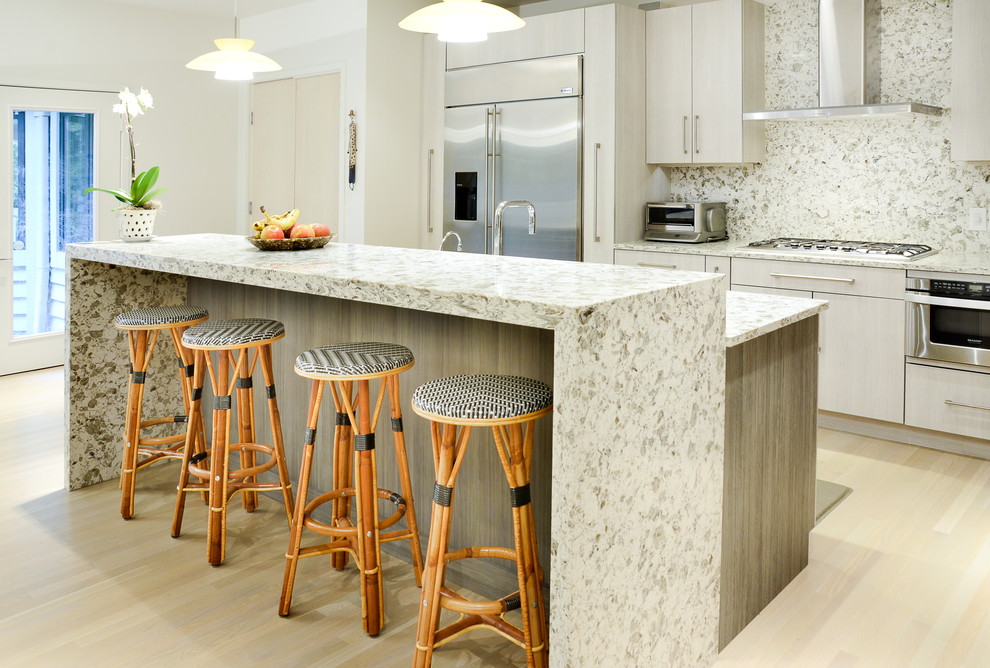 Immagine di un cucina con isola centrale minimal con ante lisce, ante grigie, elettrodomestici in acciaio inossidabile e parquet chiaro