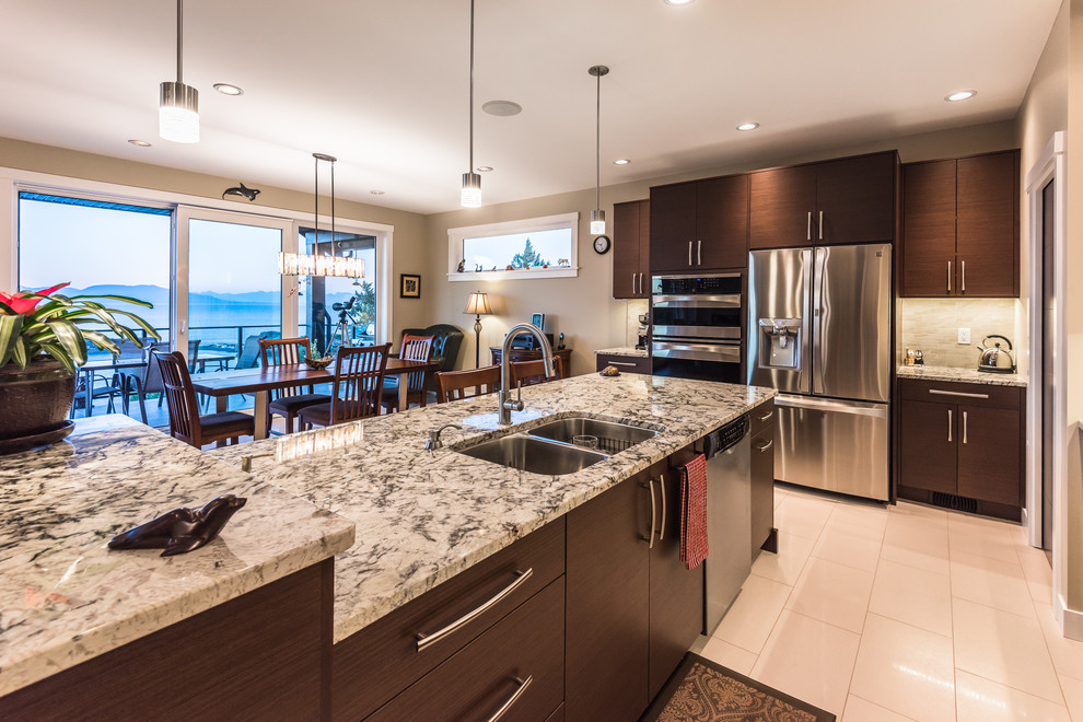 Eat-in kitchen - large traditional eat-in kitchen idea with a double-bowl sink, flat-panel cabinets, dark wood cabinets, granite countertops, beige backsplash, glass tile backsplash, stainless steel appliances and an island