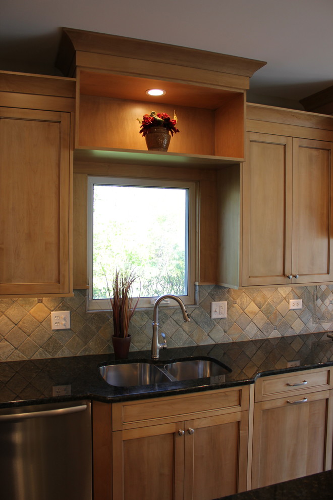 Inredning av ett klassiskt kök, med en undermonterad diskho, luckor med infälld panel, skåp i ljust trä, granitbänkskiva, grönt stänkskydd, stänkskydd i stenkakel och rostfria vitvaror