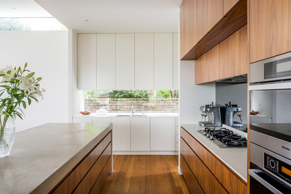 Moderne Küche in L-Form mit hellbraunen Holzschränken, braunem Holzboden, Kücheninsel, Doppelwaschbecken, flächenbündigen Schrankfronten, Rückwand-Fenster, Küchengeräten aus Edelstahl, braunem Boden und weißer Arbeitsplatte in Sydney