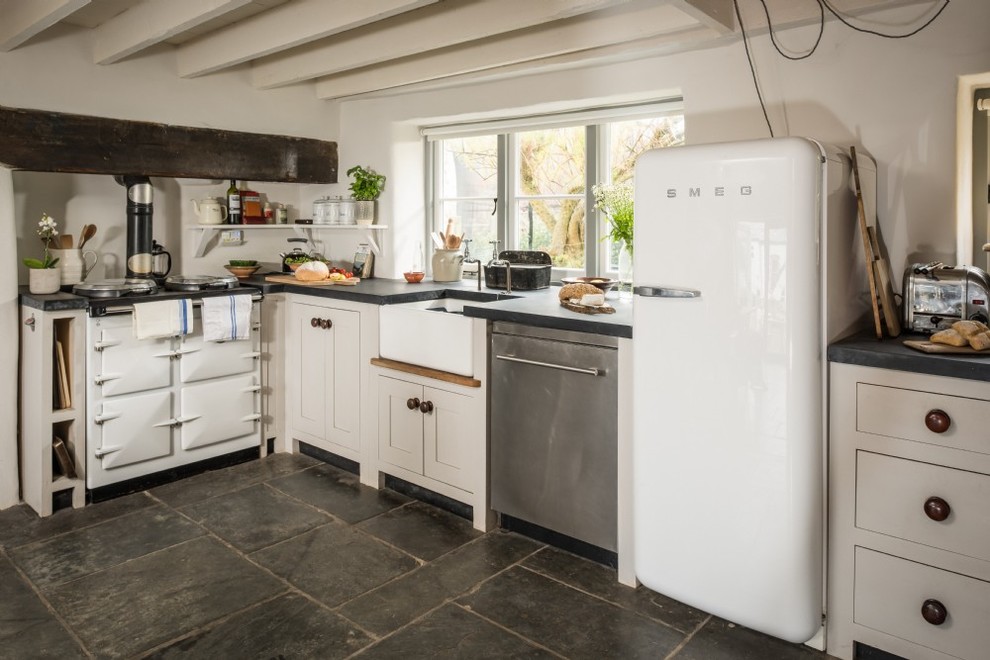 コーンウォールにある小さなカントリー風のおしゃれな独立型キッチン (エプロンフロントシンク、落し込みパネル扉のキャビネット、グレーのキャビネット、白い調理設備、グレーの床) の写真