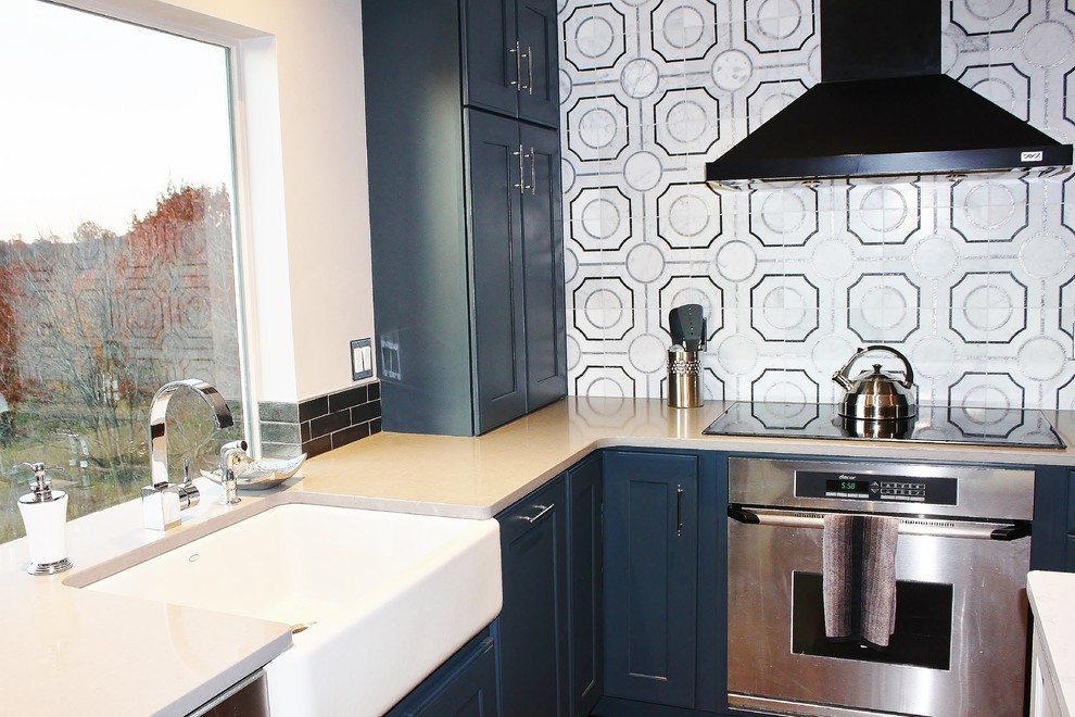 Photo of a large traditional u-shaped kitchen/diner in Philadelphia with a belfast sink, shaker cabinets, blue cabinets, engineered stone countertops, grey splashback, porcelain splashback, stainless steel appliances, dark hardwood flooring and an island.