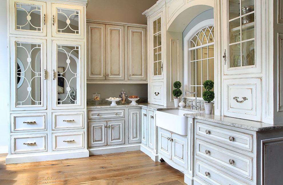 Eat-in kitchen - large traditional l-shaped medium tone wood floor and brown floor eat-in kitchen idea in Jacksonville with a farmhouse sink, glass-front cabinets, distressed cabinets, granite countertops, gray backsplash, stone slab backsplash, no island and gray countertops