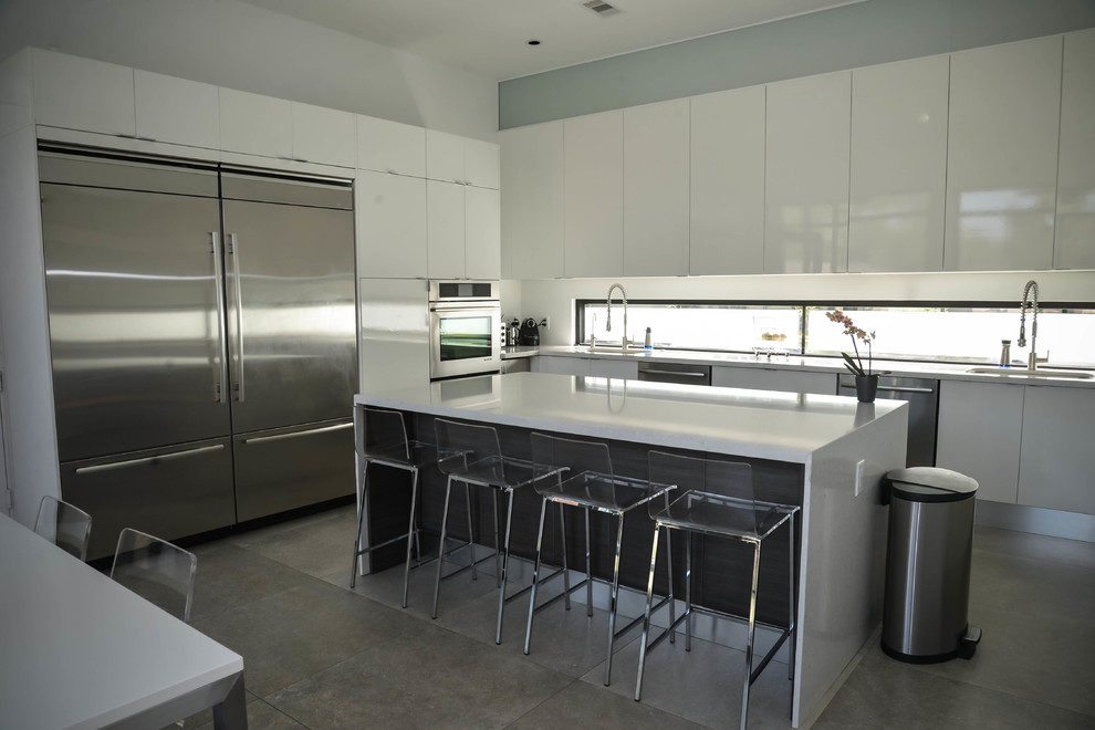 Medium sized modern l-shaped kitchen/diner in Houston with a submerged sink, flat-panel cabinets, white cabinets, composite countertops, window splashback, stainless steel appliances, porcelain flooring and an island.