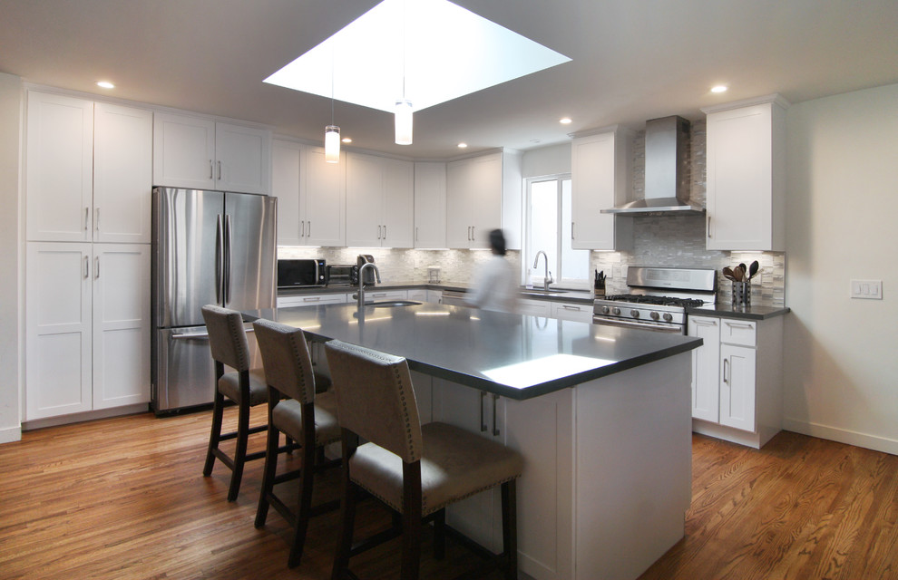 Inredning av ett modernt mellanstort grå grått kök, med en undermonterad diskho, skåp i shakerstil, vita skåp, bänkskiva i kvartsit, beige stänkskydd, stänkskydd i glaskakel, rostfria vitvaror, mellanmörkt trägolv, en köksö och brunt golv
