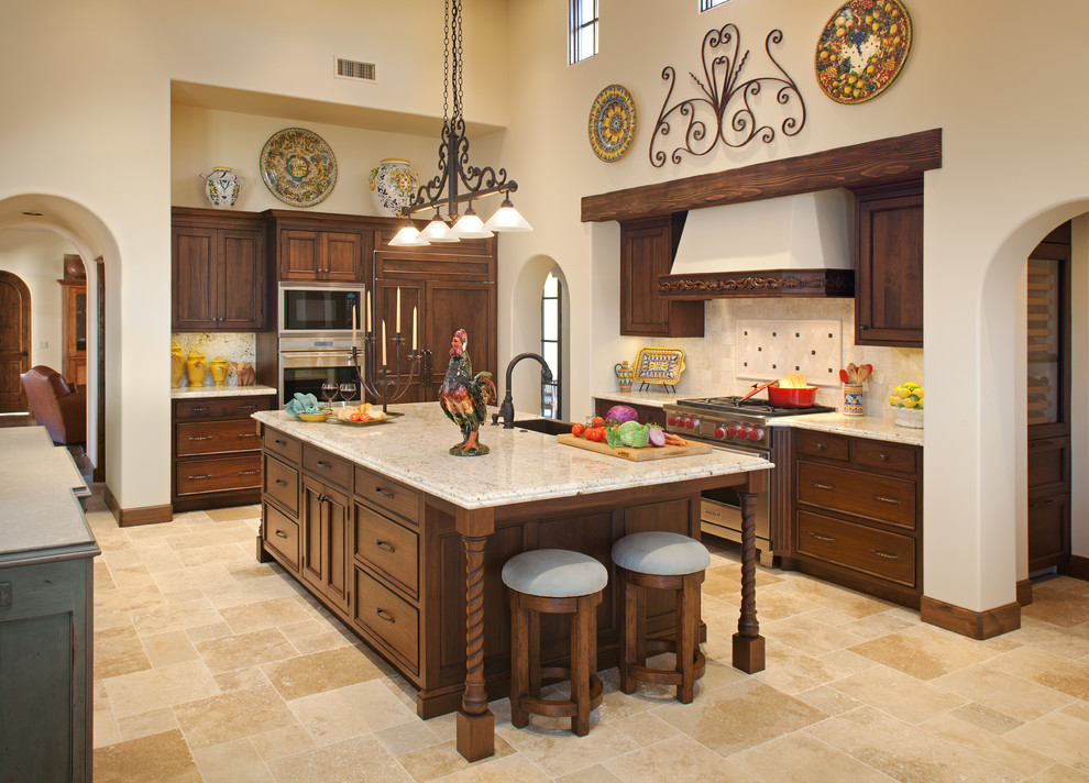 Expansive classic l-shaped open plan kitchen in San Diego with recessed-panel cabinets, dark wood cabinets, beige splashback, integrated appliances, a belfast sink, limestone flooring, granite worktops, multiple islands and limestone splashback.