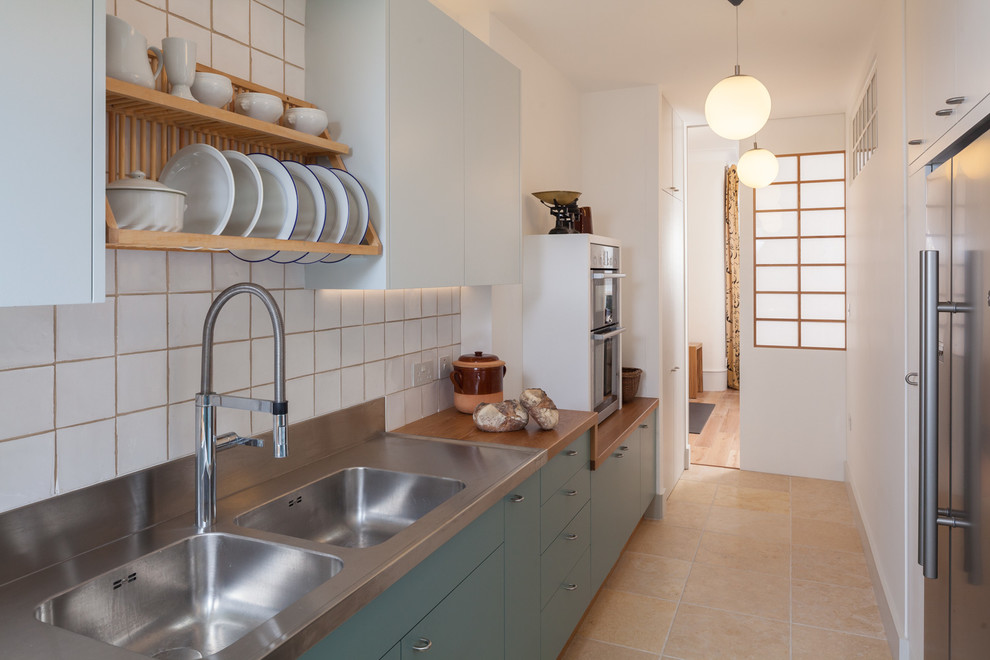 Zweizeilige, Kleine Skandinavische Küche ohne Insel mit Doppelwaschbecken, flächenbündigen Schrankfronten, Edelstahl-Arbeitsplatte und Küchenrückwand in Weiß in Gloucestershire
