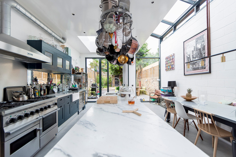 Eclectic galley kitchen/diner in London with a belfast sink, shaker cabinets, black cabinets, stainless steel appliances, concrete flooring, an island, grey floors and grey worktops.