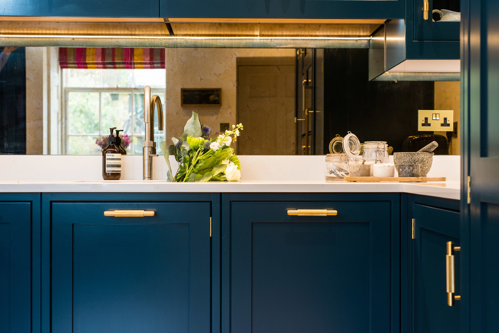 Esempio di una cucina moderna di medie dimensioni con lavello da incasso, ante in stile shaker, ante blu, top in superficie solida, paraspruzzi a specchio, elettrodomestici in acciaio inossidabile, parquet chiaro, penisola e top bianco