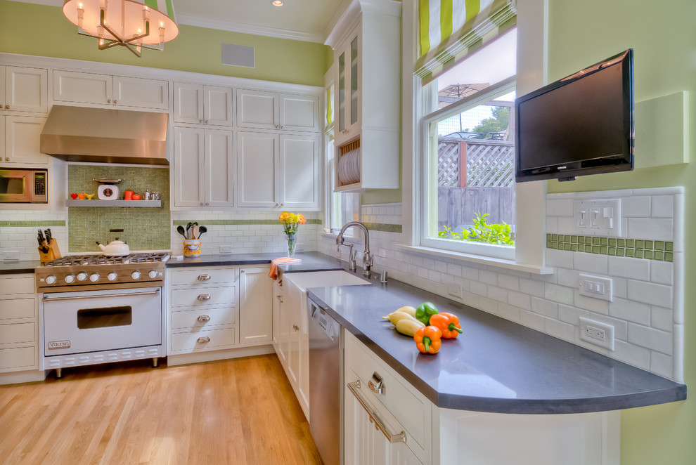 Example of a trendy l-shaped kitchen design in San Francisco with white appliances, a farmhouse sink, quartz countertops, shaker cabinets, white cabinets, green backsplash and subway tile backsplash