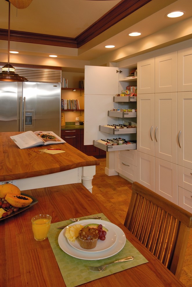 Ejemplo de cocina comedor exótica con electrodomésticos de acero inoxidable, encimera de madera, armarios estilo shaker, puertas de armario blancas, suelo de corcho y barras de cocina
