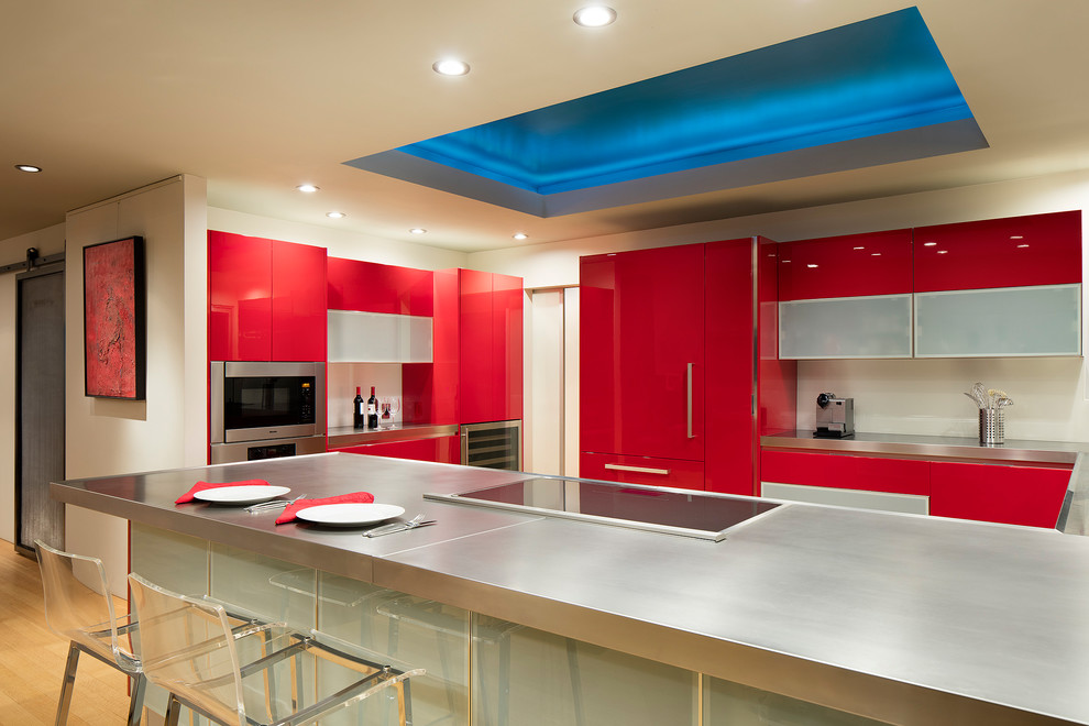 Example of a mid-sized trendy u-shaped light wood floor and brown floor eat-in kitchen design in San Francisco with a single-bowl sink, flat-panel cabinets, red cabinets, stainless steel countertops, white backsplash, glass sheet backsplash, stainless steel appliances, a peninsula and gray countertops