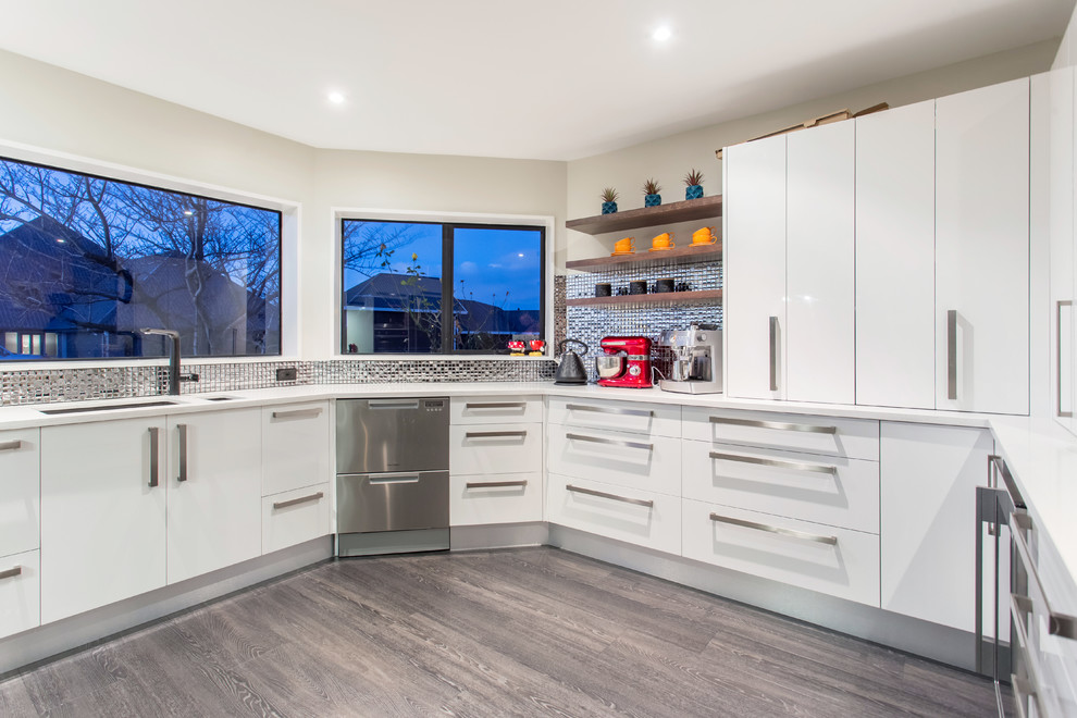 Photo of a large modern u-shaped enclosed kitchen in Christchurch with a submerged sink, flat-panel cabinets, white cabinets, grey splashback, mosaic tiled splashback, stainless steel appliances, laminate floors, a breakfast bar, grey floors and white worktops.