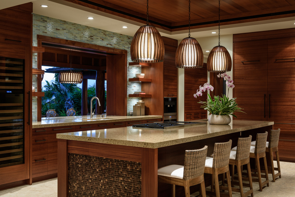 This is an example of a large world-inspired u-shaped open plan kitchen in Hawaii with a submerged sink, flat-panel cabinets, medium wood cabinets, engineered stone countertops, blue splashback, glass tiled splashback, integrated appliances, limestone flooring and an island.