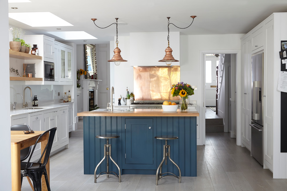 Example of an urban eat-in kitchen design in London with an undermount sink, shaker cabinets, white cabinets, metallic backsplash, metal backsplash, stainless steel appliances and an island