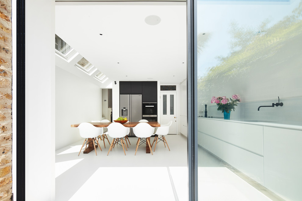 This is an example of a medium sized contemporary l-shaped kitchen/diner in London with a built-in sink, flat-panel cabinets, white cabinets, white splashback, black appliances, no island and white floors.