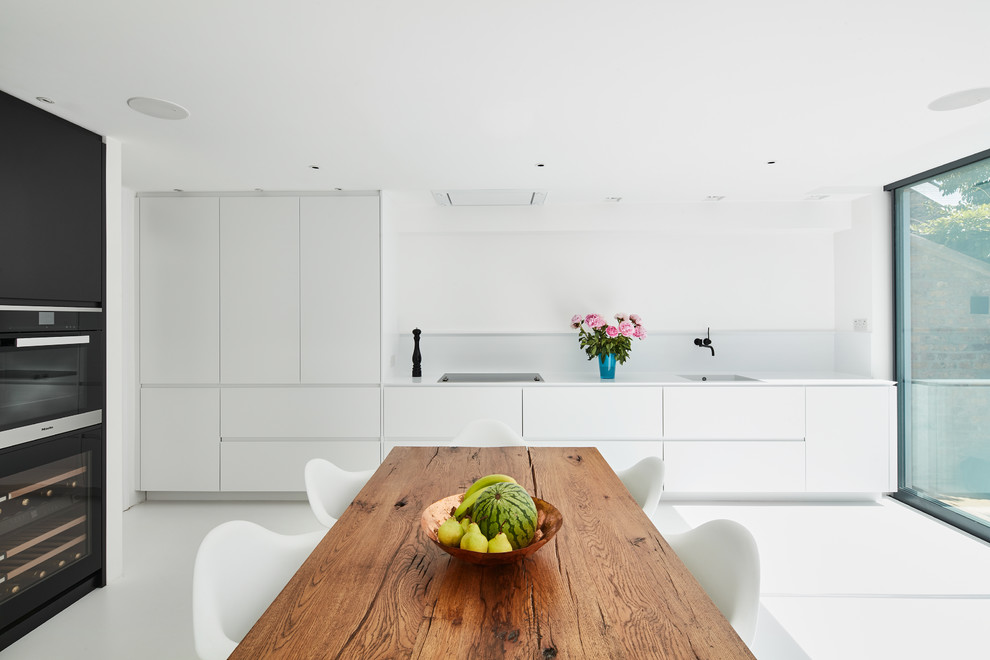 Inspiration for a medium sized contemporary l-shaped kitchen/diner in London with a built-in sink, flat-panel cabinets, white cabinets, white splashback, black appliances, no island and white floors.
