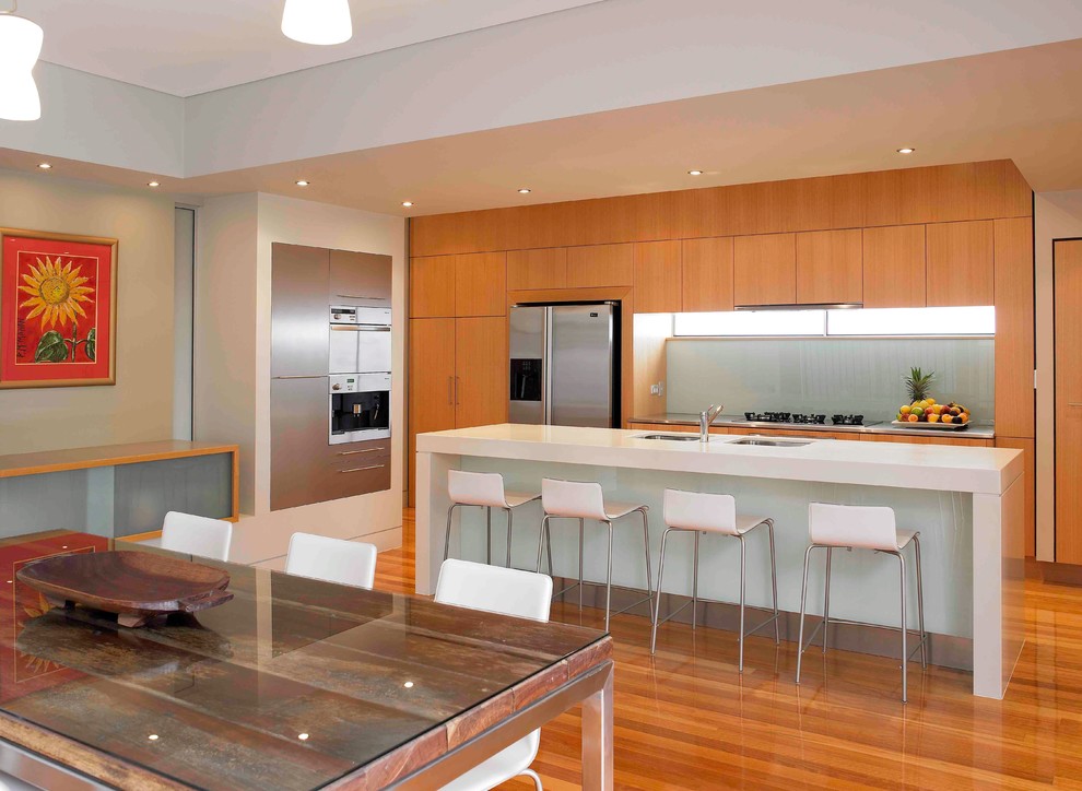 Zweizeilige Moderne Wohnküche mit Unterbauwaschbecken, flächenbündigen Schrankfronten, hellbraunen Holzschränken, Quarzwerkstein-Arbeitsplatte, Glasrückwand und Küchengeräten aus Edelstahl in Brisbane