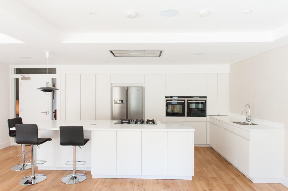 Moderne Küche in L-Form mit flächenbündigen Schrankfronten, weißen Schränken, Küchengeräten aus Edelstahl, braunem Holzboden und Kücheninsel in Glasgow