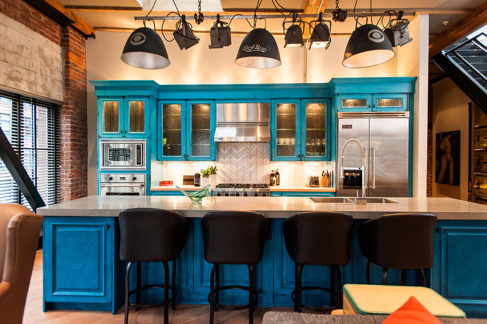 Photo of an industrial galley open plan kitchen in Vancouver with concrete worktops, stainless steel appliances, glass-front cabinets, distressed cabinets and beige splashback.