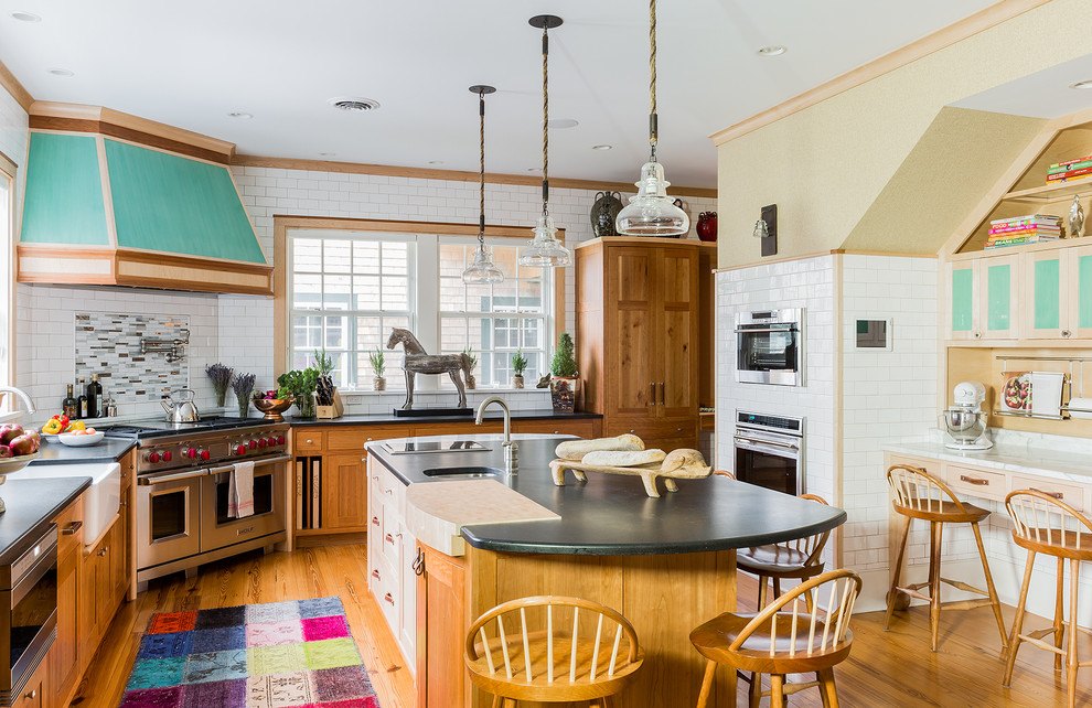 Example of a large classic l-shaped medium tone wood floor and brown floor kitchen design in Boston with an island, a farmhouse sink, shaker cabinets, light wood cabinets, white backsplash, subway tile backsplash, stainless steel appliances and granite countertops