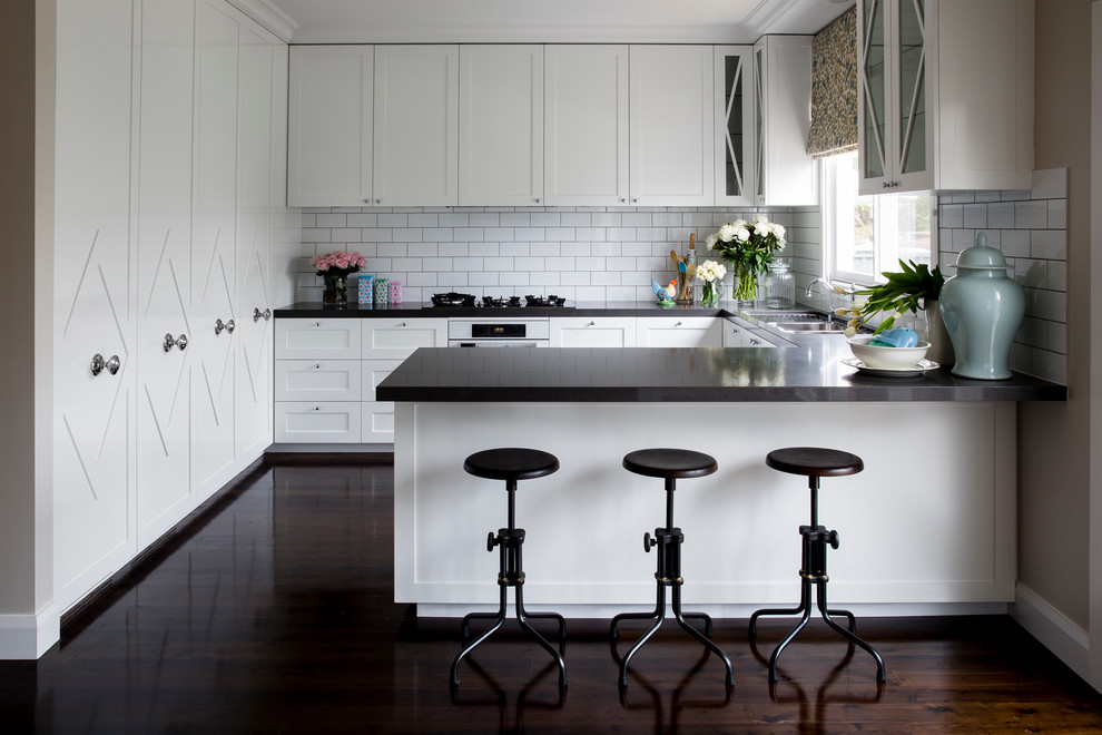 Klassische Küche in U-Form mit weißen Schränken, Schrankfronten mit vertiefter Füllung, Küchenrückwand in Weiß, Rückwand aus Metrofliesen und weißen Elektrogeräten in Sydney