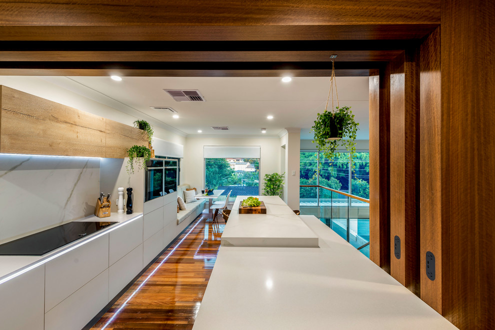 This is an example of a large contemporary l-shaped kitchen/diner in Brisbane with a submerged sink, flat-panel cabinets, beige cabinets, engineered stone countertops, white splashback, stone slab splashback, black appliances, medium hardwood flooring, an island, multi-coloured floors and yellow worktops.