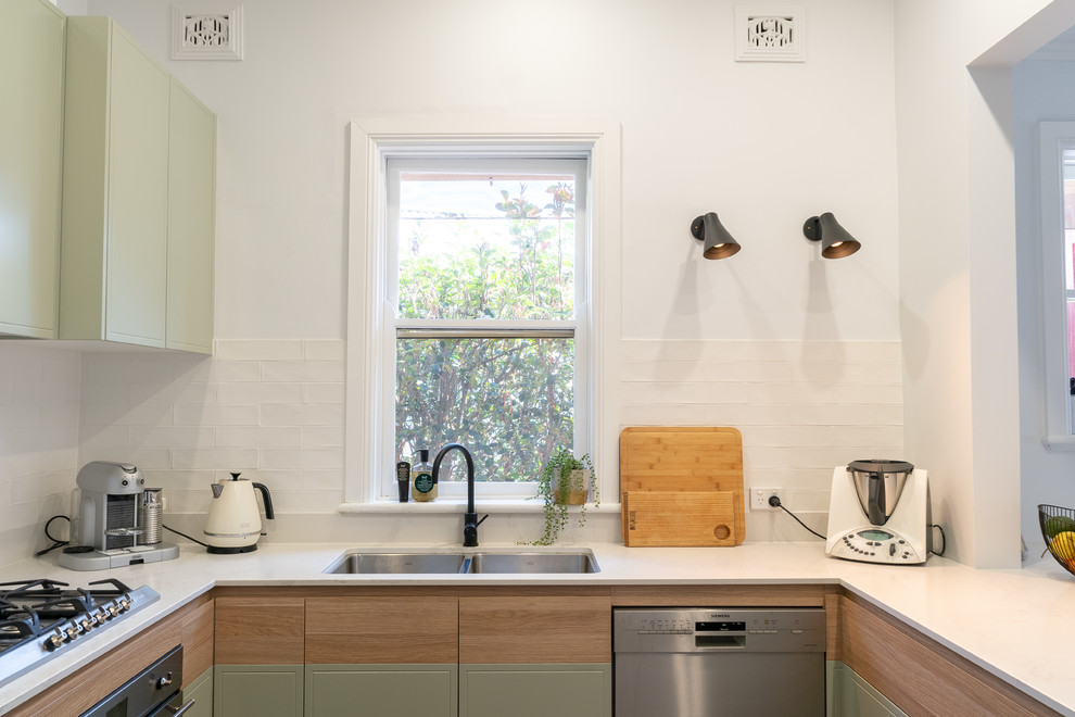 Modern inredning av ett mellanstort vit vitt kök, med släta luckor, gröna skåp, bänkskiva i kvarts, vitt stänkskydd, stänkskydd i tunnelbanekakel, rostfria vitvaror, en halv köksö och en dubbel diskho