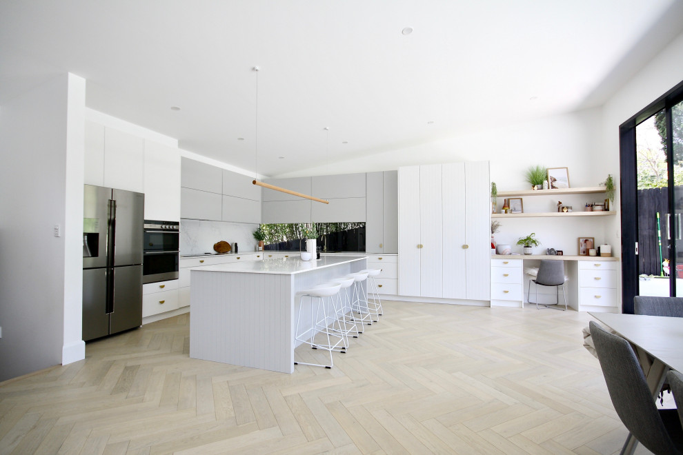 Inredning av ett modernt stort vit vitt kök, med en undermonterad diskho, släta luckor, vita skåp, bänkskiva i kvarts, vitt stänkskydd, stänkskydd i sten, rostfria vitvaror, mellanmörkt trägolv, en köksö och brunt golv