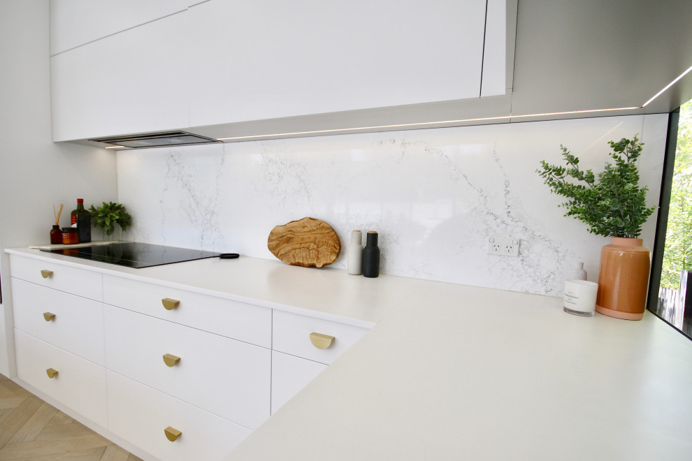 Inspiration for a large modern l-shaped open plan kitchen in Sydney with a submerged sink, flat-panel cabinets, white cabinets, engineered stone countertops, white splashback, stone slab splashback, stainless steel appliances, medium hardwood flooring, an island, brown floors and white worktops.