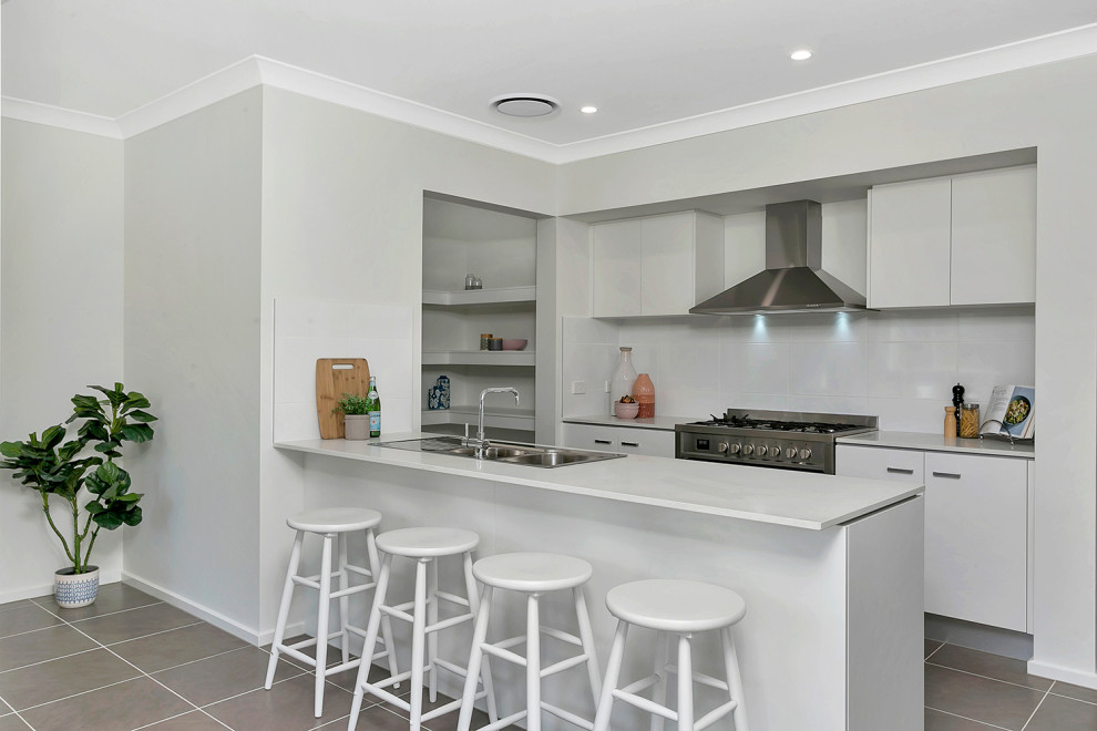 Design ideas for a medium sized contemporary kitchen in Central Coast with a built-in sink, flat-panel cabinets, white cabinets, white splashback, stainless steel appliances, a breakfast bar, grey floors and white worktops.