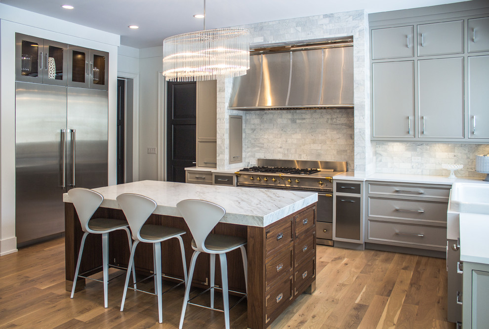 Photo of a traditional u-shaped kitchen in Chicago with recessed-panel cabinets, grey cabinets, stone tiled splashback, stainless steel appliances, medium hardwood flooring, an island and grey splashback.