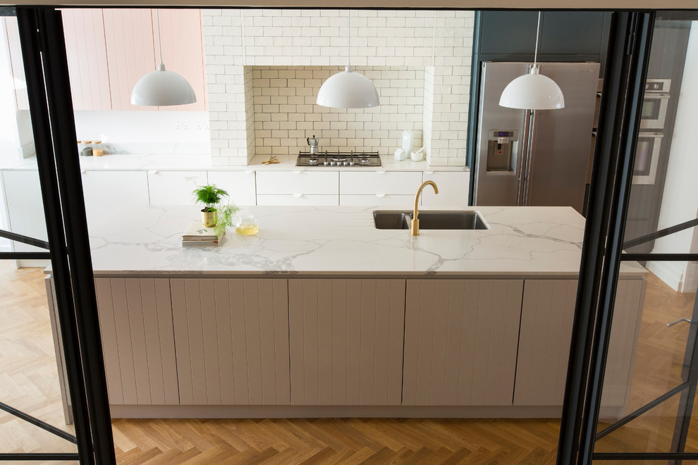 Modern inredning av ett mycket stort vit vitt kök, med en integrerad diskho, luckor med profilerade fronter, grå skåp, marmorbänkskiva, vitt stänkskydd, stänkskydd i tunnelbanekakel, rostfria vitvaror, mellanmörkt trägolv, en köksö och brunt golv