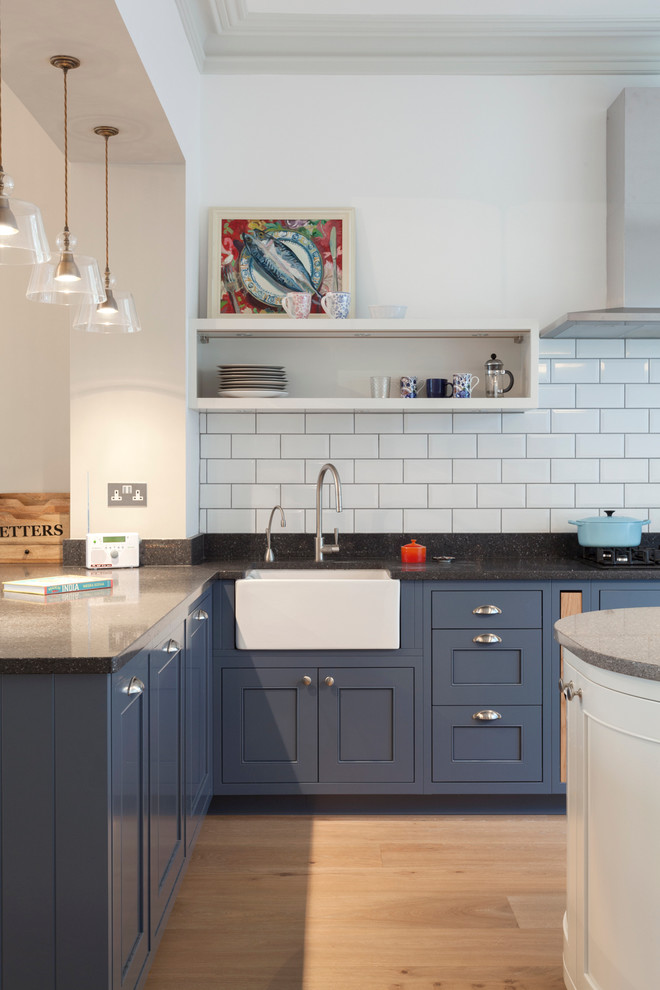 Photo of a medium sized contemporary kitchen/diner in London with a belfast sink, beaded cabinets, blue cabinets, granite worktops, white splashback, metro tiled splashback and an island.