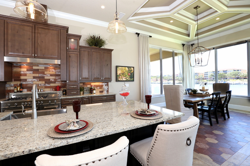 Eat-in kitchen - large traditional single-wall porcelain tile and multicolored floor eat-in kitchen idea in Orlando with a farmhouse sink, raised-panel cabinets, brown cabinets, granite countertops, multicolored backsplash, brick backsplash, stainless steel appliances and an island