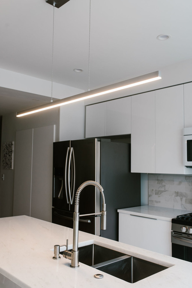 Small modern single-wall kitchen/diner in Baltimore with a double-bowl sink, flat-panel cabinets, white cabinets, marble worktops, white splashback, marble splashback, stainless steel appliances, light hardwood flooring, an island, beige floors and white worktops.
